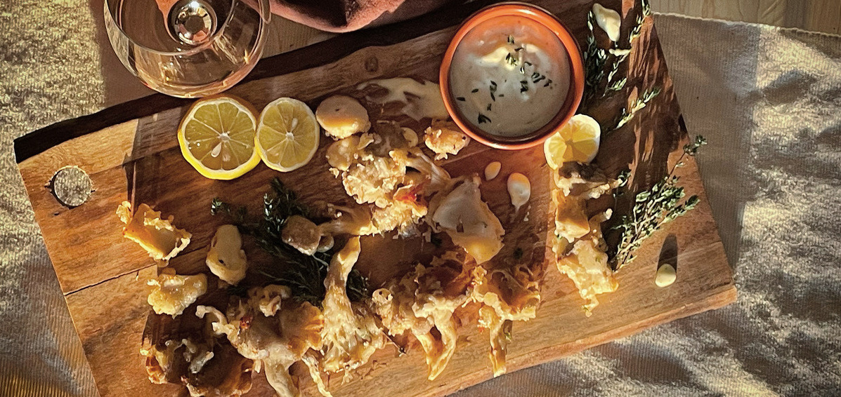 An overhead view of a pile of fried mushrooms on a wood board, a  glass of white wine beside it
