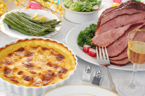 A white tables spread with ham, quiche, asparagus and salad with white wine glasses