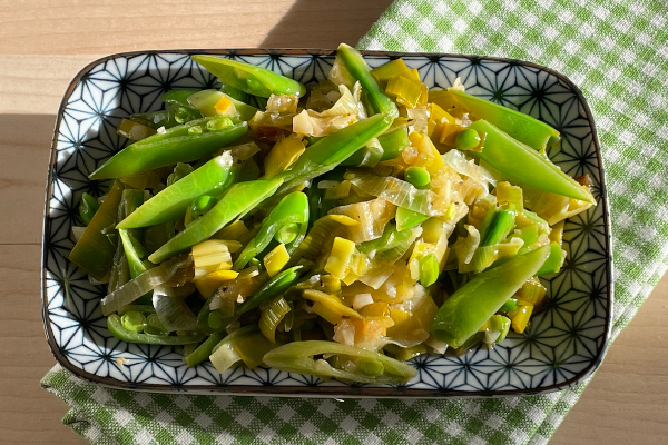 sautéed leeks and peas on a blue and white plate in the sun