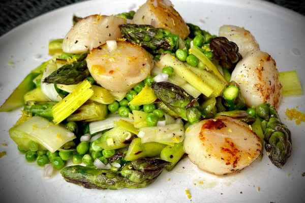 side view of seared scallops and asparagus on a white plate