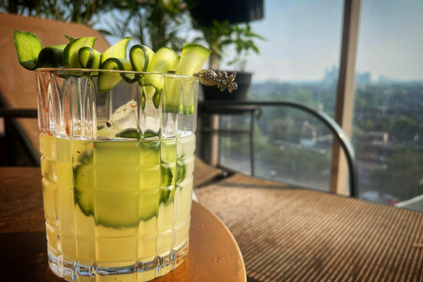 side view of a rocks glass with a yellow cocktail and cucumber garnish