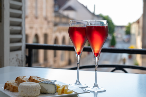 Two flutes of purple cocktails on a table in front of an open window with a European background