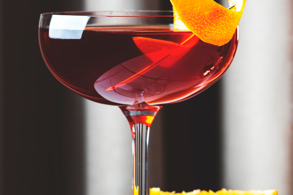 close up of a red cocktail in a coup with an orange twist