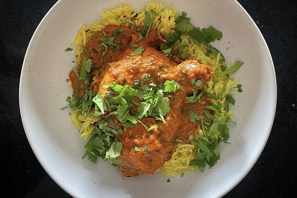 Overhead view of a red saucy chicken breast on yellow rice with green cilantro scatter over top.