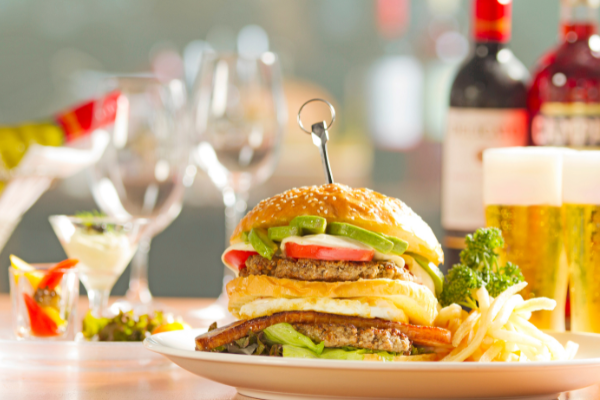 Side view of a huge hamburger on a plate, a bottle of red and a bottle of white wine behind it