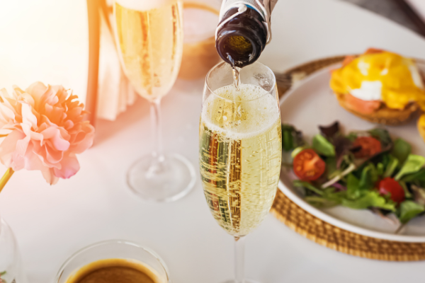 Champagne pouring into a glass beside a plate of eggs benedict
