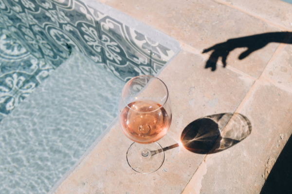 Overhead view of a glass of rosé by a pool with the shadow of a hand reaching for the glass