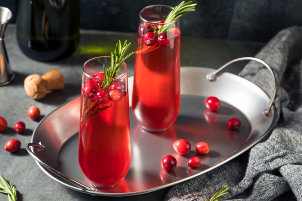 two stemless glasses filled with red cocktails on a silver tray with scattered cranberries around it