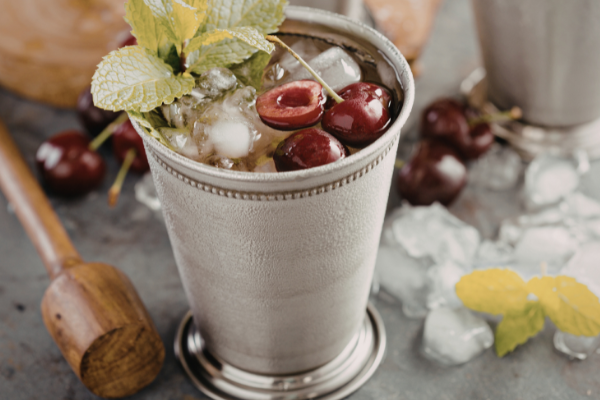 cocktail in a ti cup garnished with cherries and mint