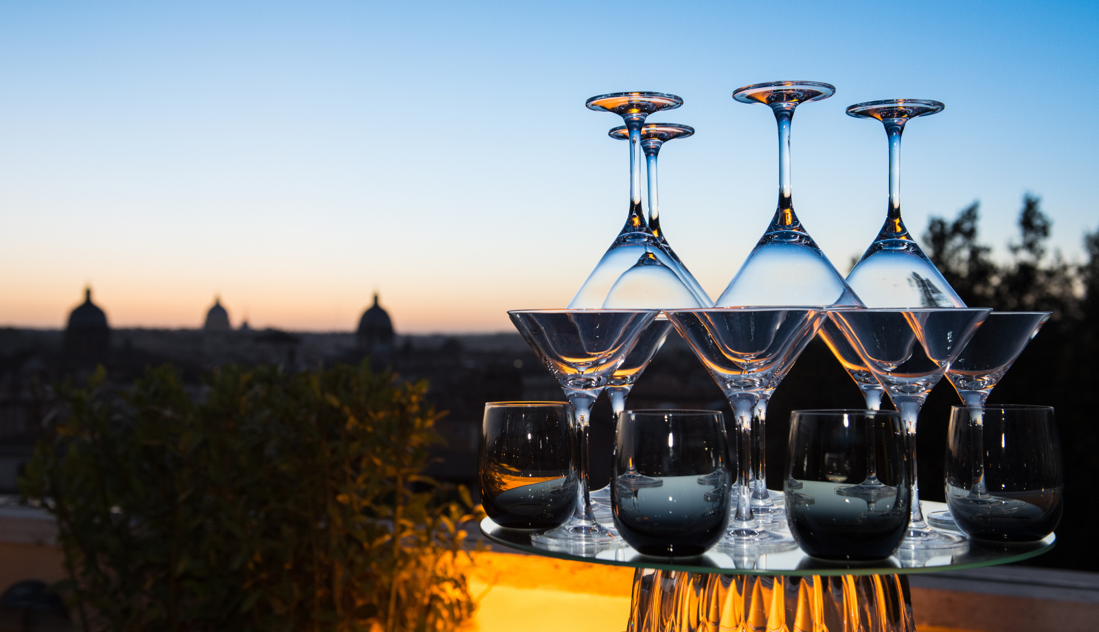 a stack of martini glasses on an outdoor table at dusk. The City scape in the background
