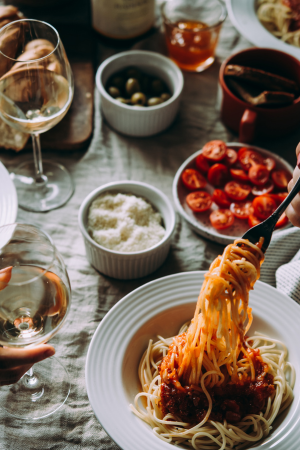 Swirling spaghetti on a fork over a big bowl of pasta, white wine glasses scatter on the table