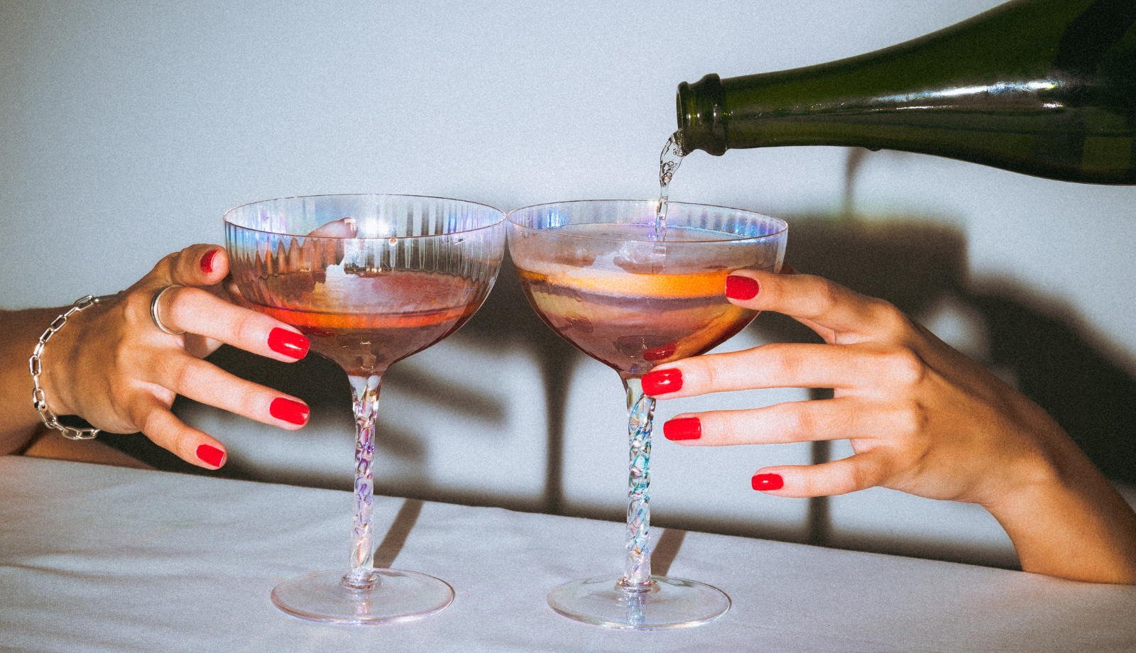 two hands with long red nails reaching for coups being filled with bubbly