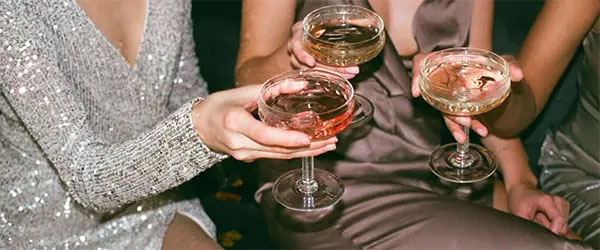 close up on three champagne coups held by glamorous women clinking